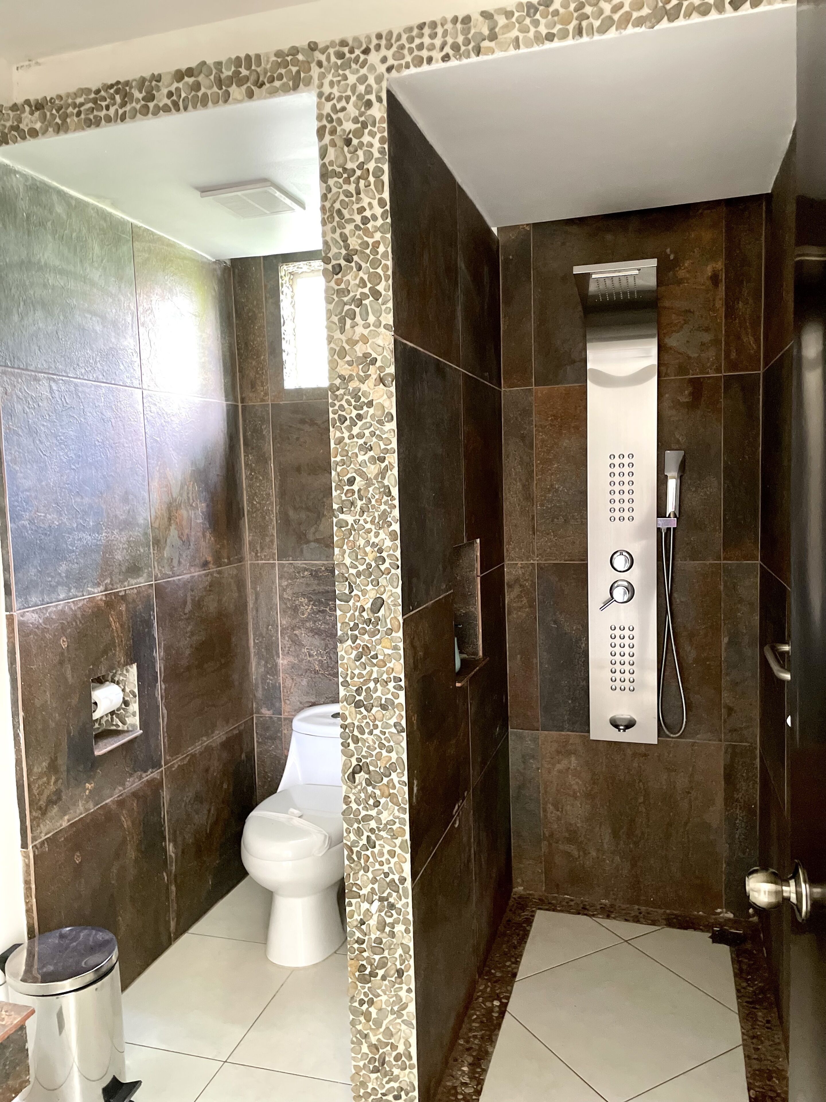 A bathroom with a shower, toilet, and trash bin.