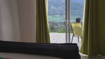 Une chambre à coucher avec un lit, une chaise et une vue sur une colline, visible par la fenêtre.