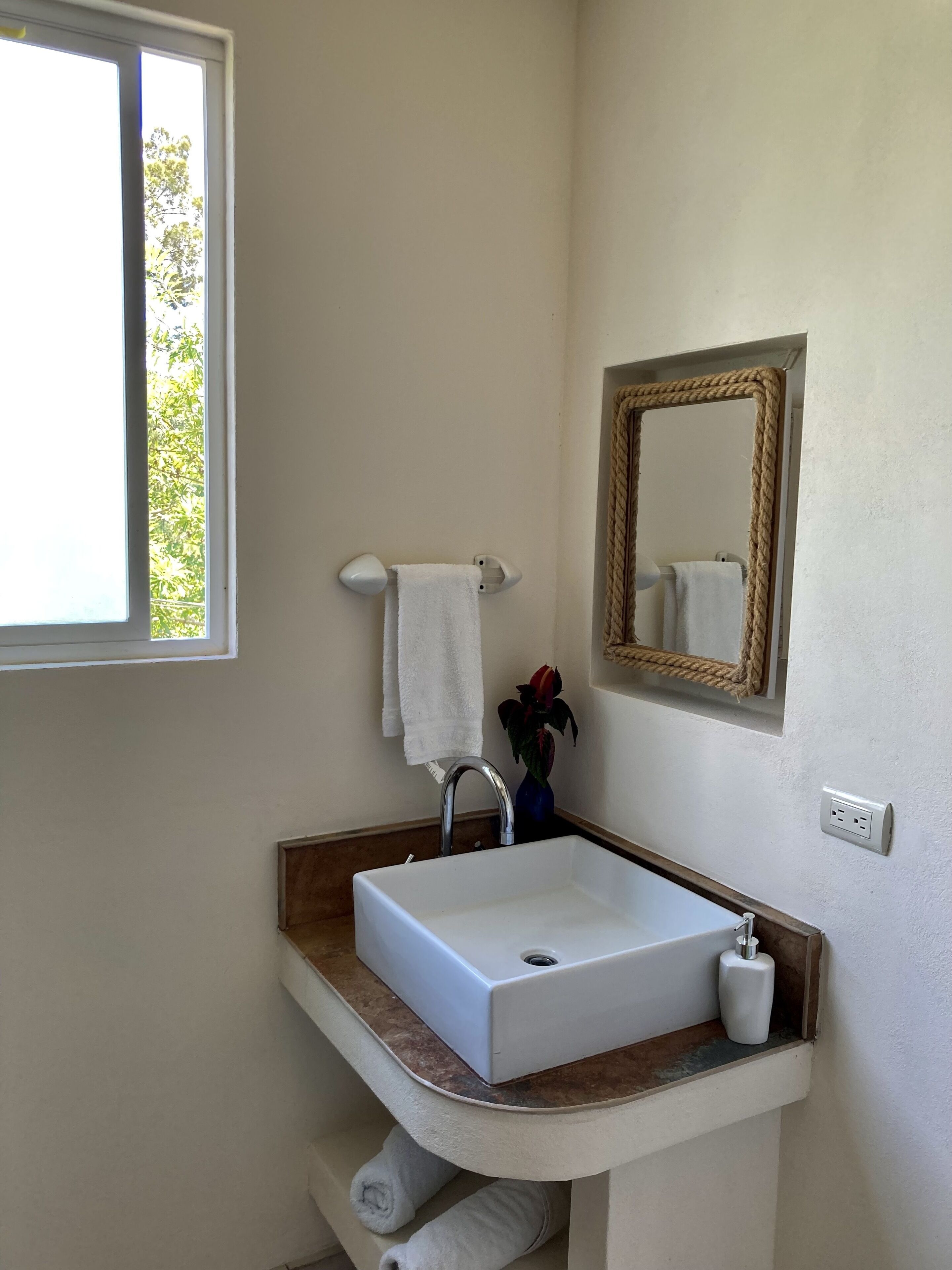 Een badkamer met een wit wastafelmeubel, een spiegel en een raam.