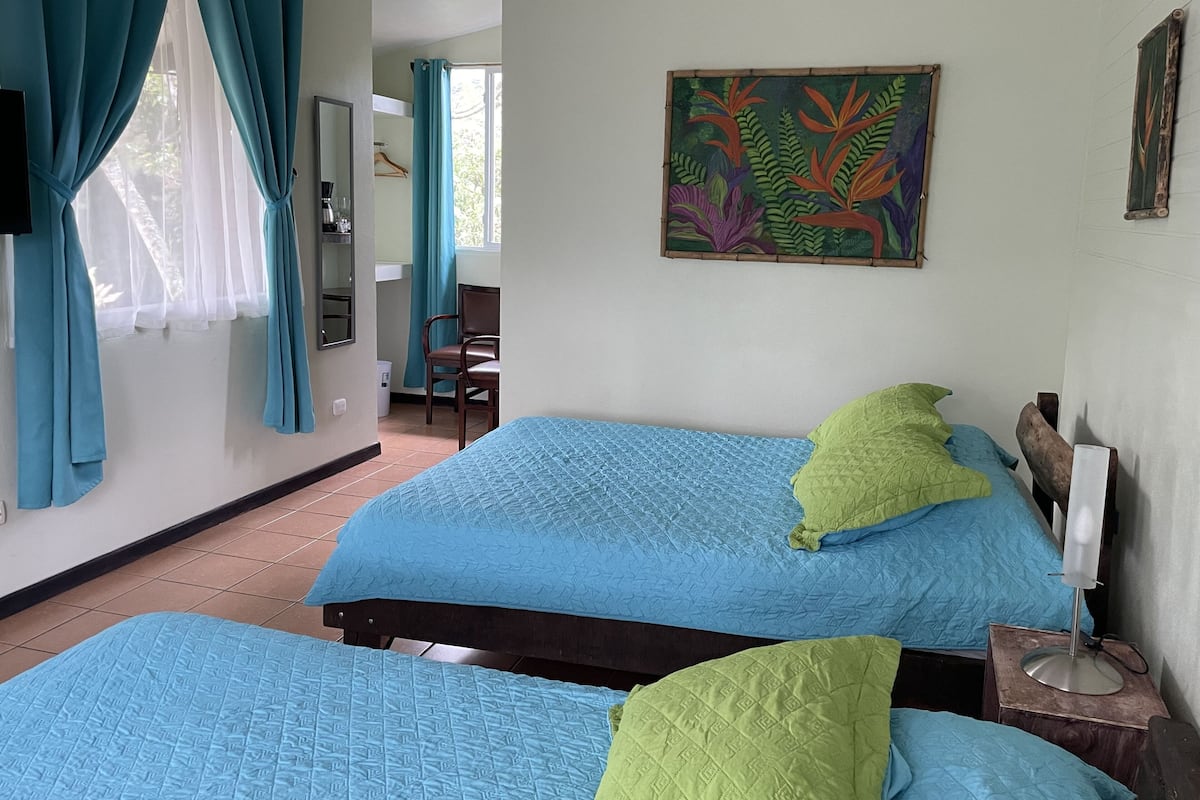 A room with two beds, a chair, a desk, and a painting on the wall.
