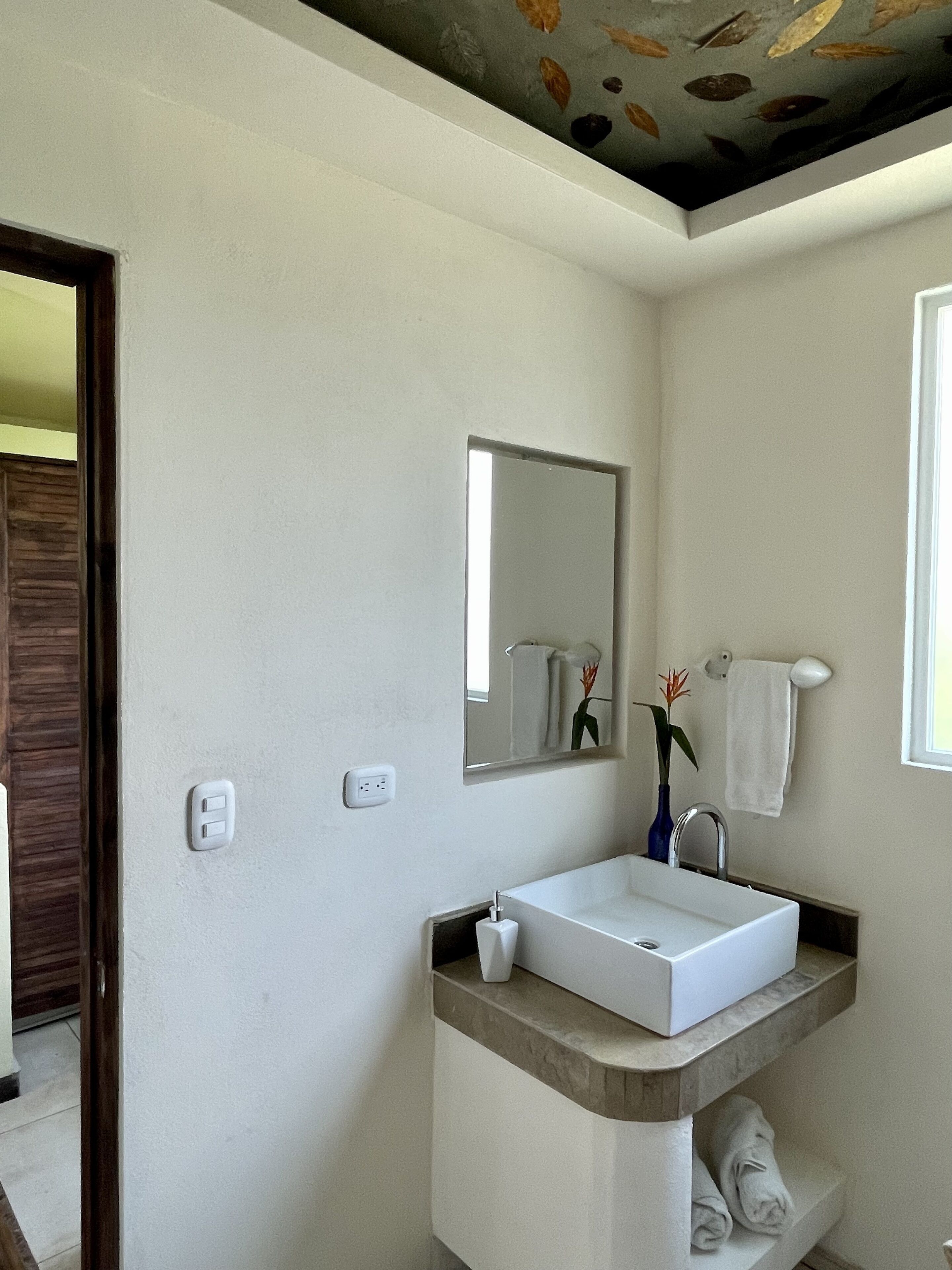 Un baño moderno con un lavamanos blanco, un espejo y un perchero para toallas.
