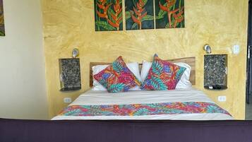 A bed with a floral bedspread, two pillows with a tropical pattern, and three wall-mounted paintings of tropical plants.