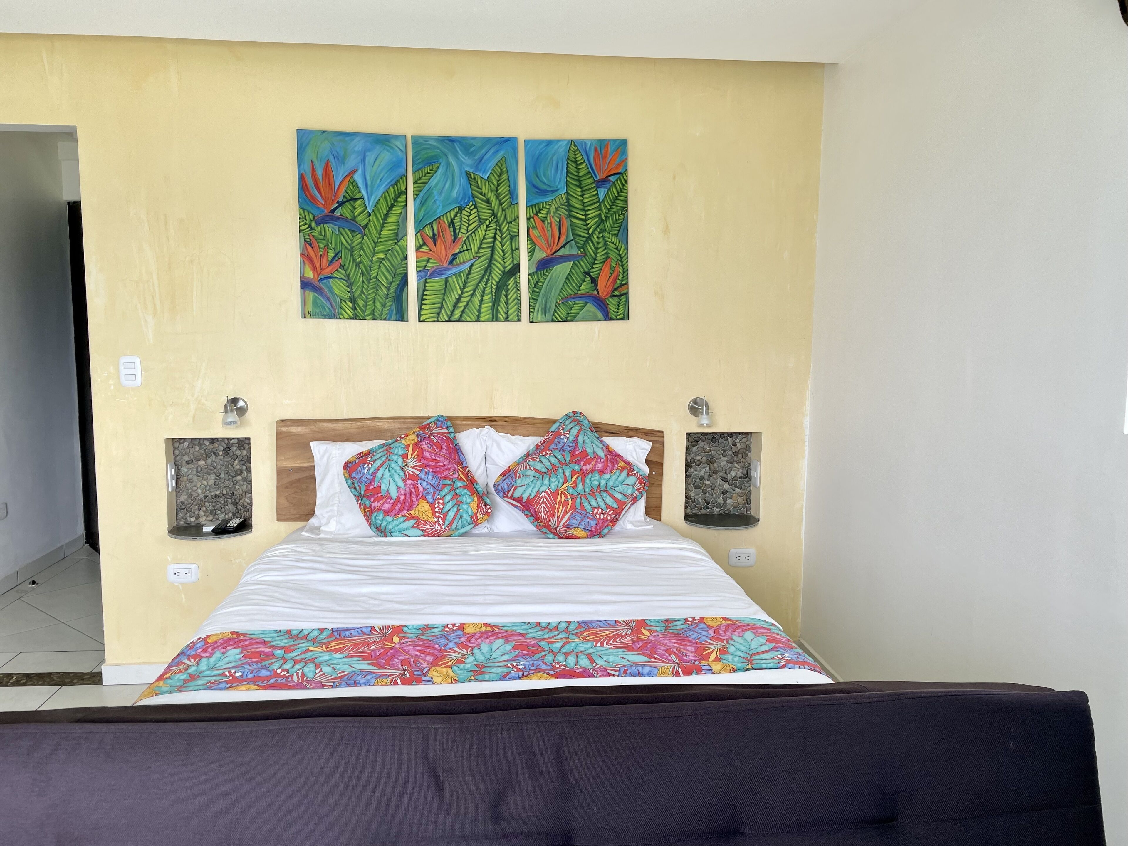 A bed with a floral bedspread, a wooden headboard, and two wall-mounted lamps.