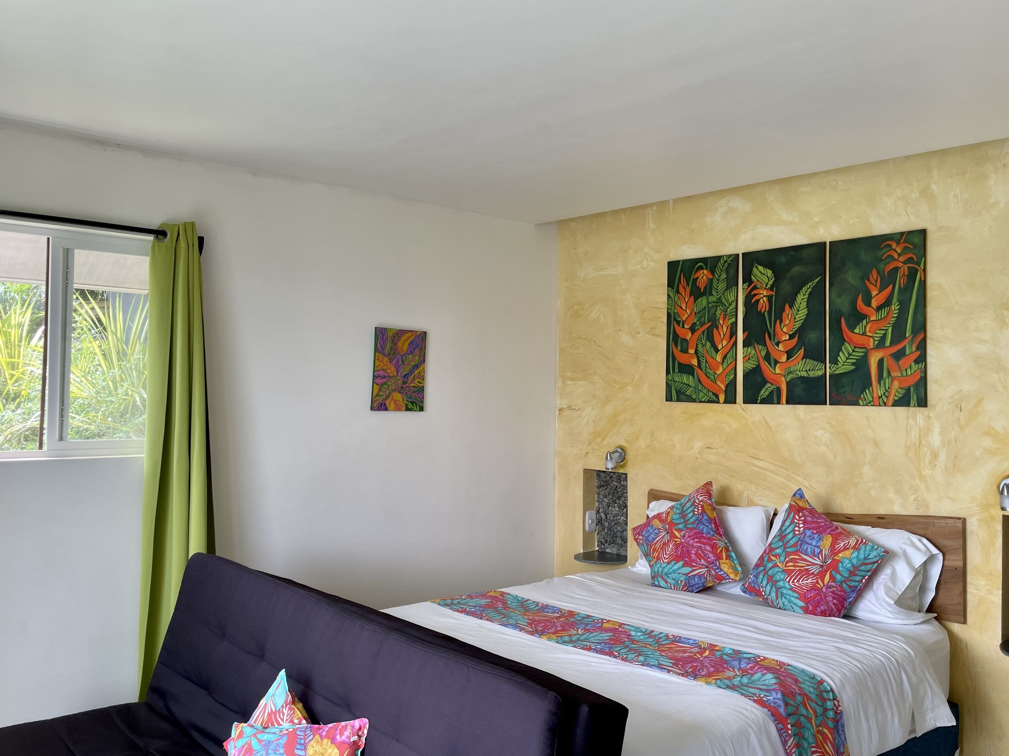 Habitació d'hotel amb un llit, un sofà, una finestra amb cortines i tres quadres penjats a la paret.