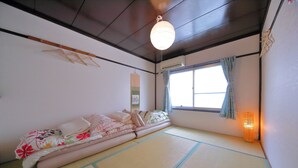 A tatami mat room with a futon bed, a hanging light fixture, and a window with a curtain.