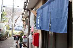 Une rue étroite où est garé un vélo sur le bord, avec une boîte de raccordement rouge et un tissu bleu qui pend à un bâtiment.