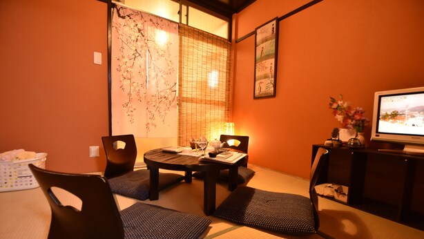 A traditional Japanese-style room with tatami flooring, a low table with cushions, a television, and a decorative screen.