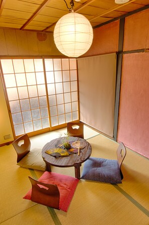 Una habitación japonesa tradicional con suelo de tatami, un biombio shoji, una mesa redonda con un abanico y un farol de papel colgante.