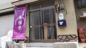 A building with a purple banner, a metal gate, a brick wall, and a potted plant. - Oyado Tofukuji (Kyoto)