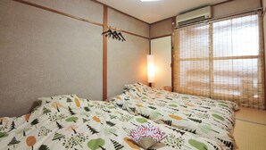 A hotel room with a bed, a wall-mounted air conditioner, a window with bamboo blinds, and a bedside lamp. - Oyado Shogoin (Kyoto)