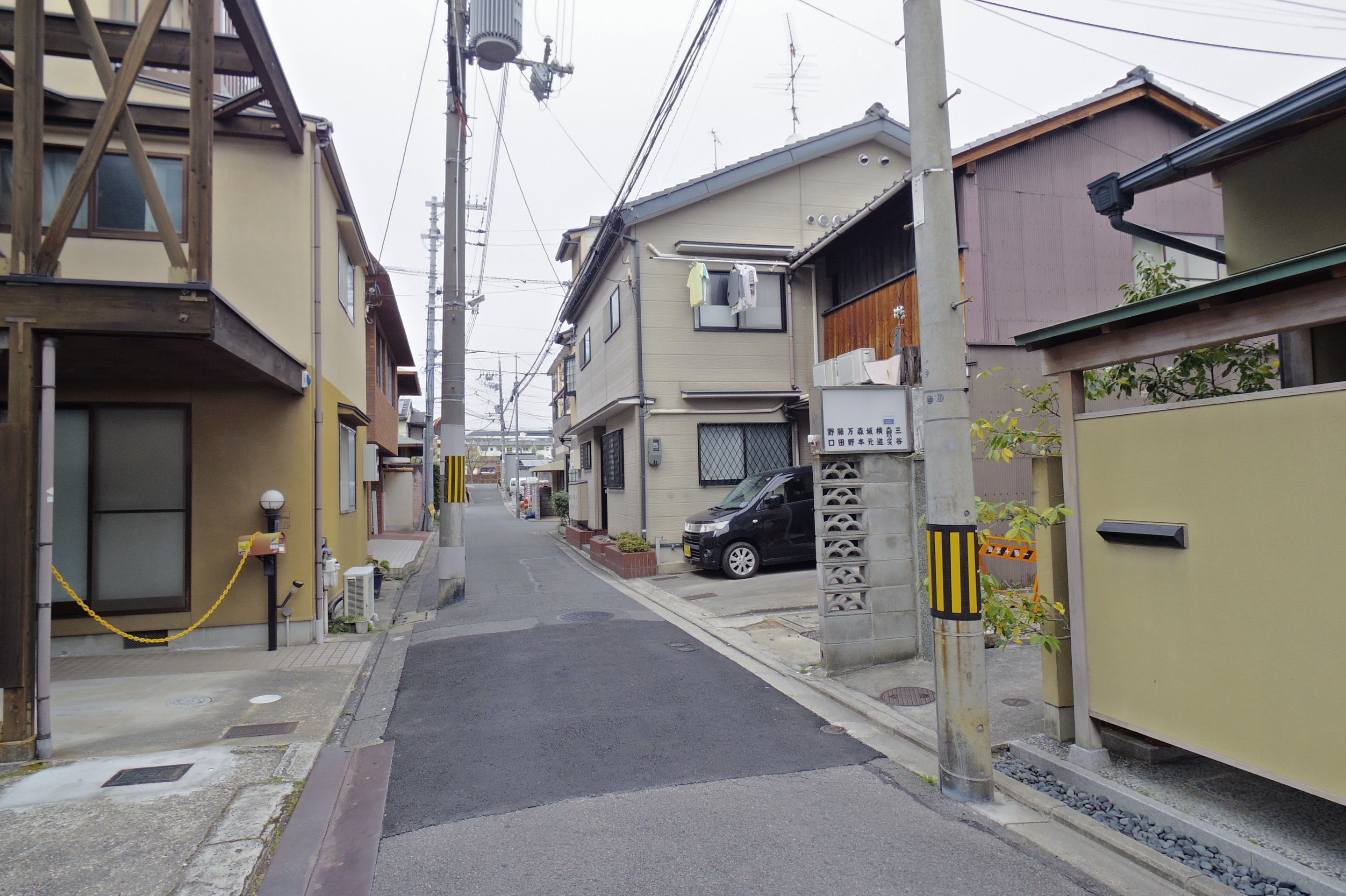 A narrow urban street lined with residential buildings, featuring a black car parked on the side.