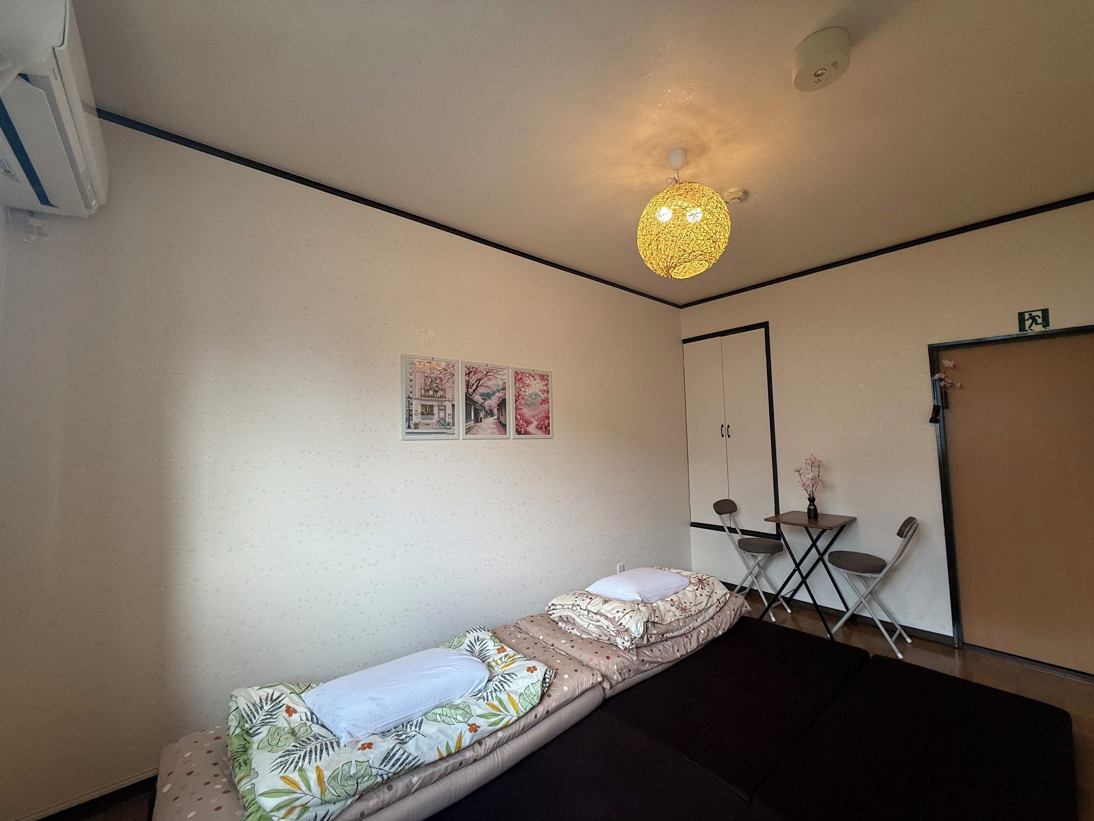 A single bed with a floral bedspread, a small table with a vase, and a ceiling light fixture.