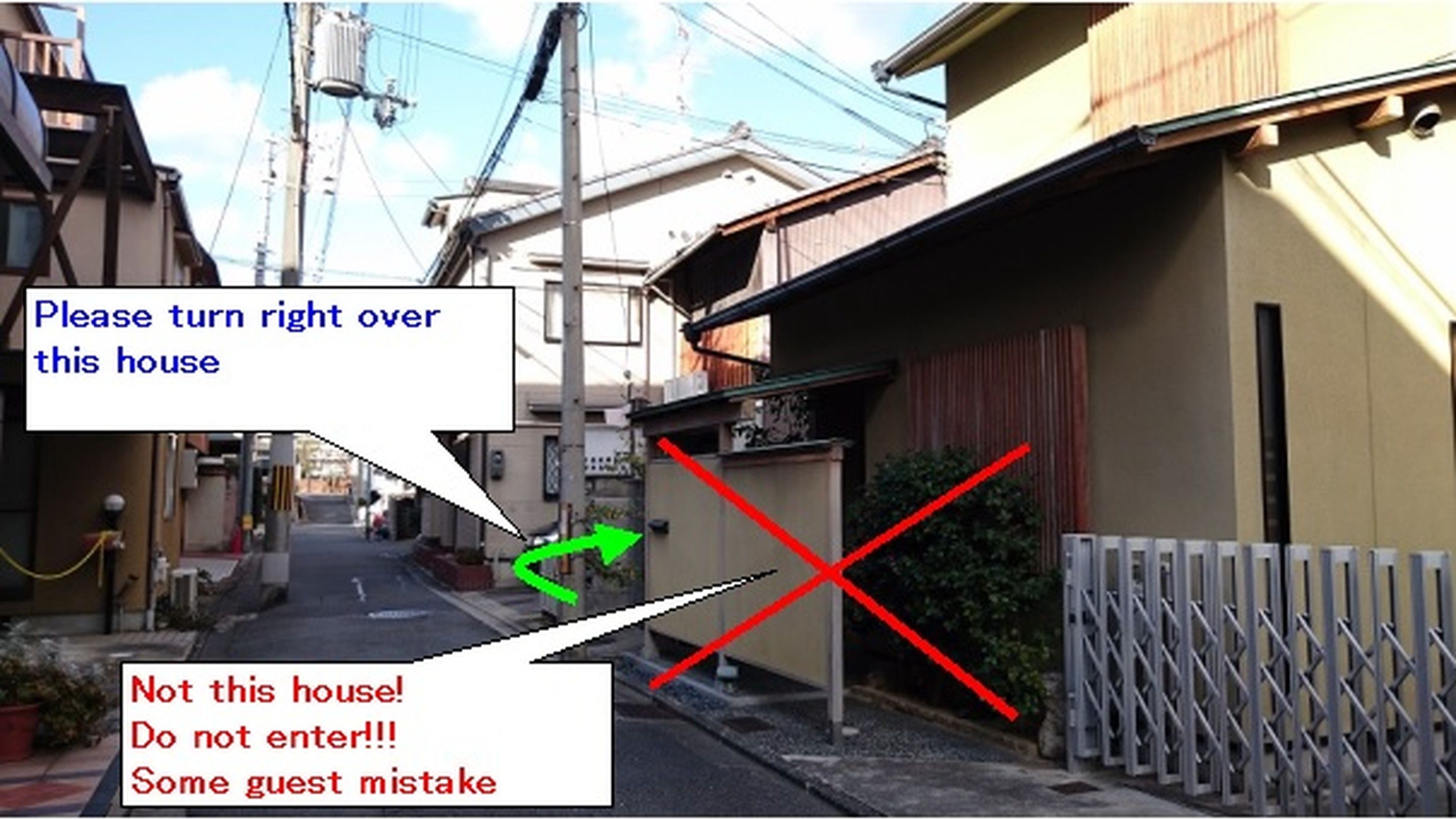 A narrow street with houses on both sides, a gated area with a red 'X' marking, and a green arrow indicating a direction.