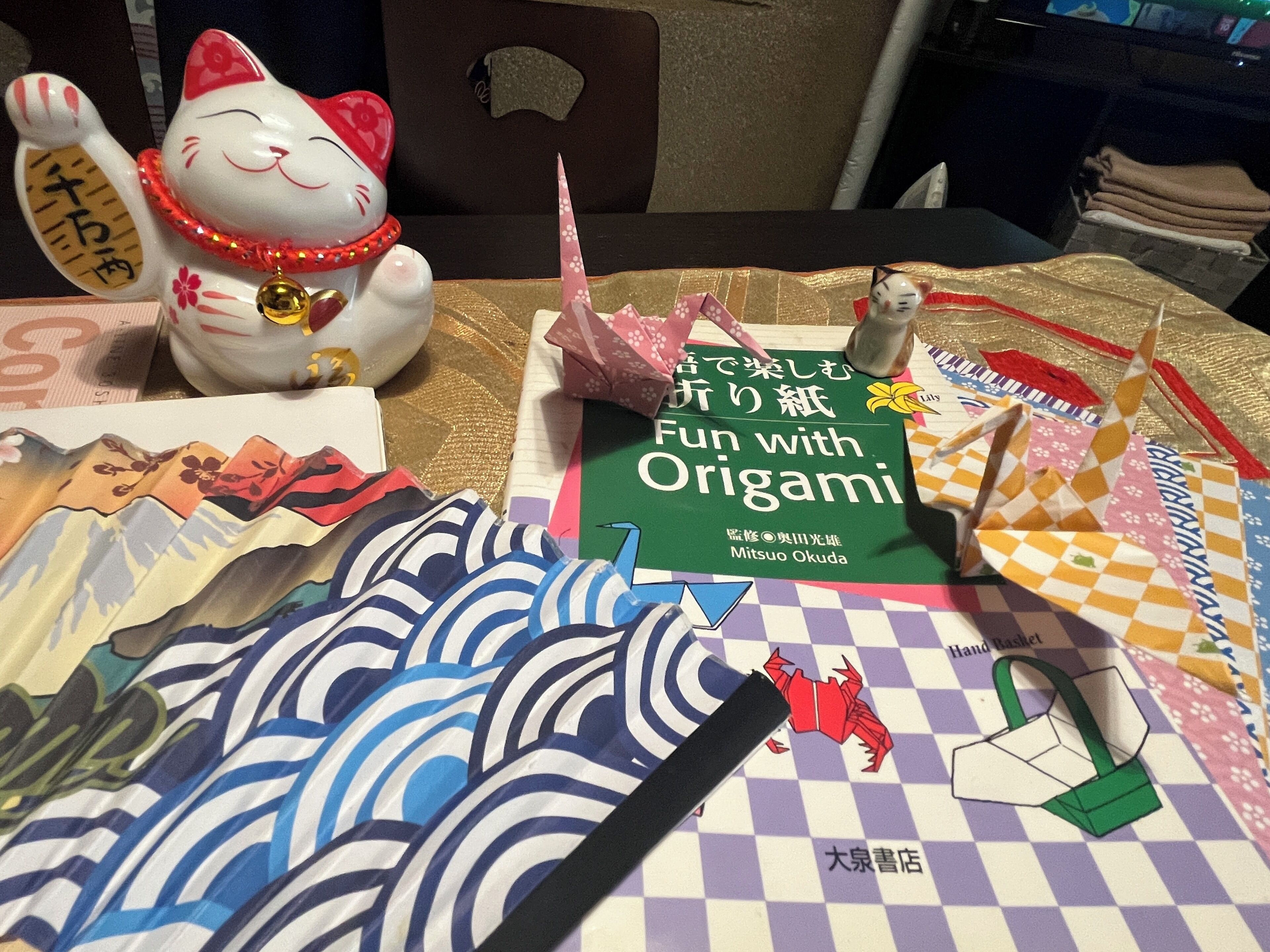 Pöydällä on origamikirjoja, kissahahmo ja origamista tehtyjä malleja.