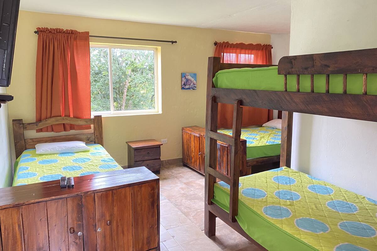 Une chambre avec des lits superposés, une armoire en bois, une petite table de chevet et une fenêtre avec des rideaux.