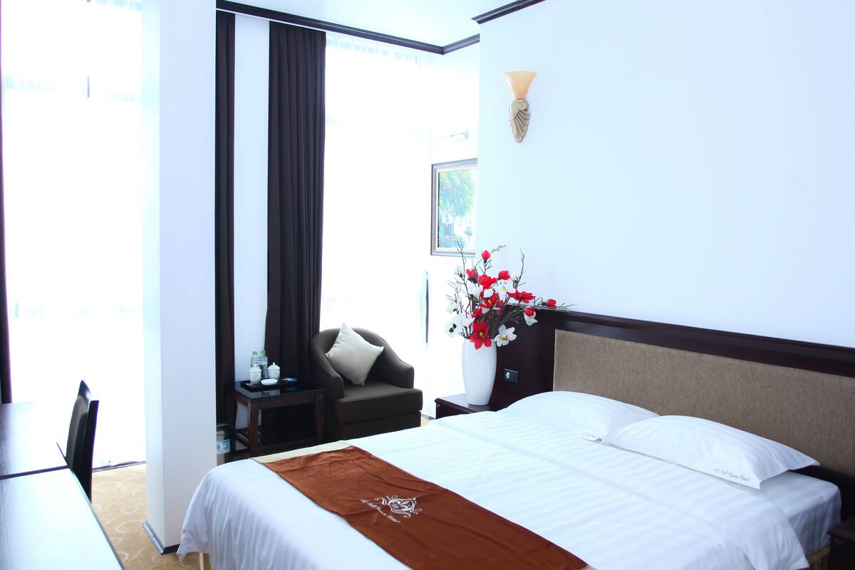 A hotel room with a bed, a desk, a chair, and a vase of flowers.