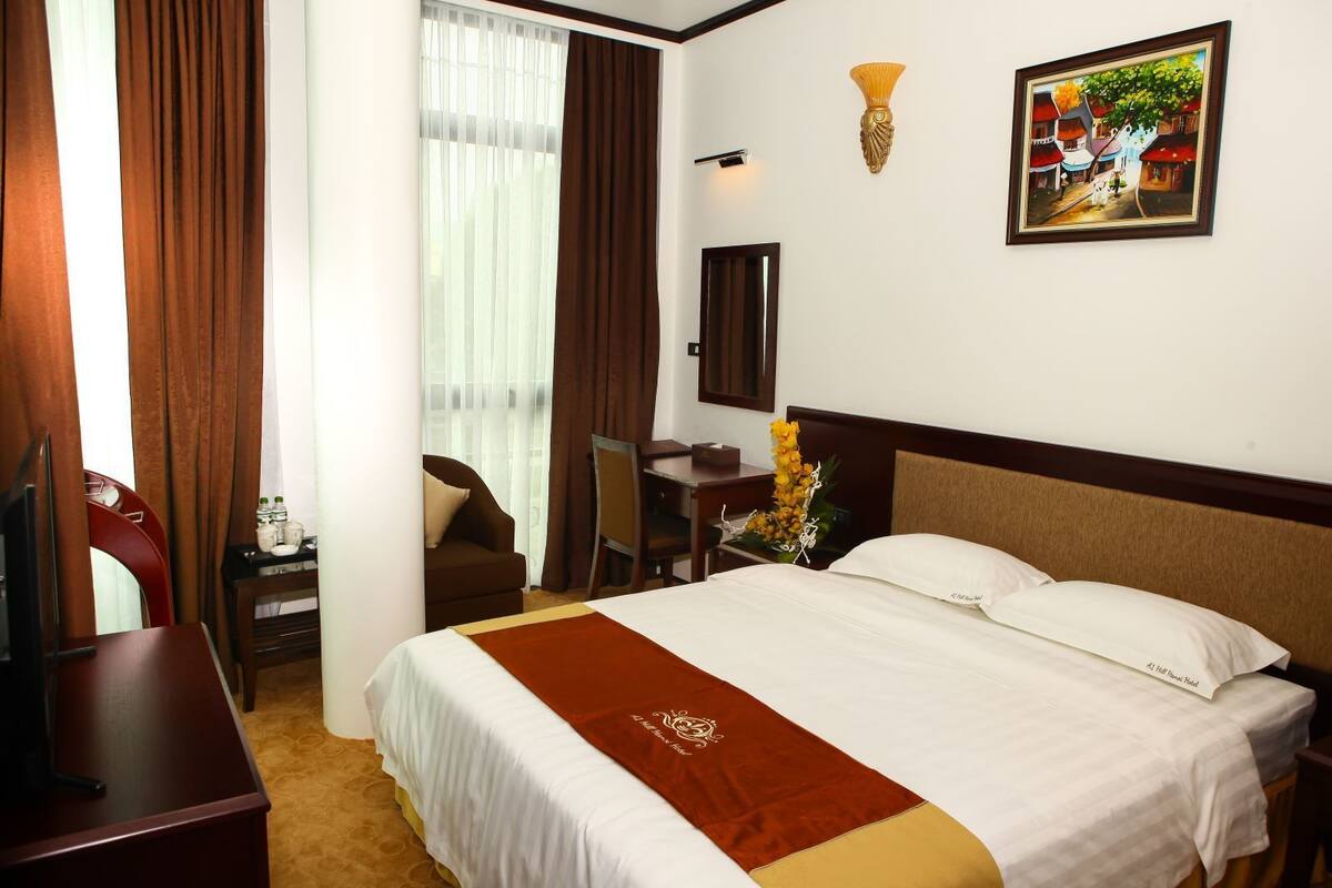 A hotel room with a bed, a desk, a chair, a TV, and a painting on the wall.