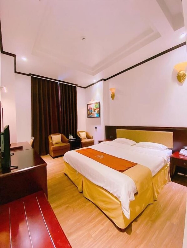 A hotel room with a bed, a desk, a chair, a television, and a painting on the wall.