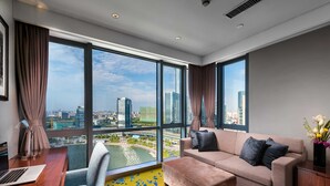 Une chambre d’hôtel moderne dotée d’une grande fenêtre donnant sur la ville, d’un canapé, d’un bureau avec un ordinateur portable et d’un petit tapis.