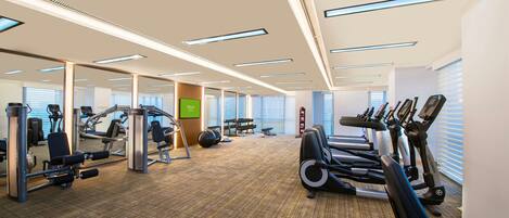 A gym with exercise equipment, mirrors, and a carpeted floor.