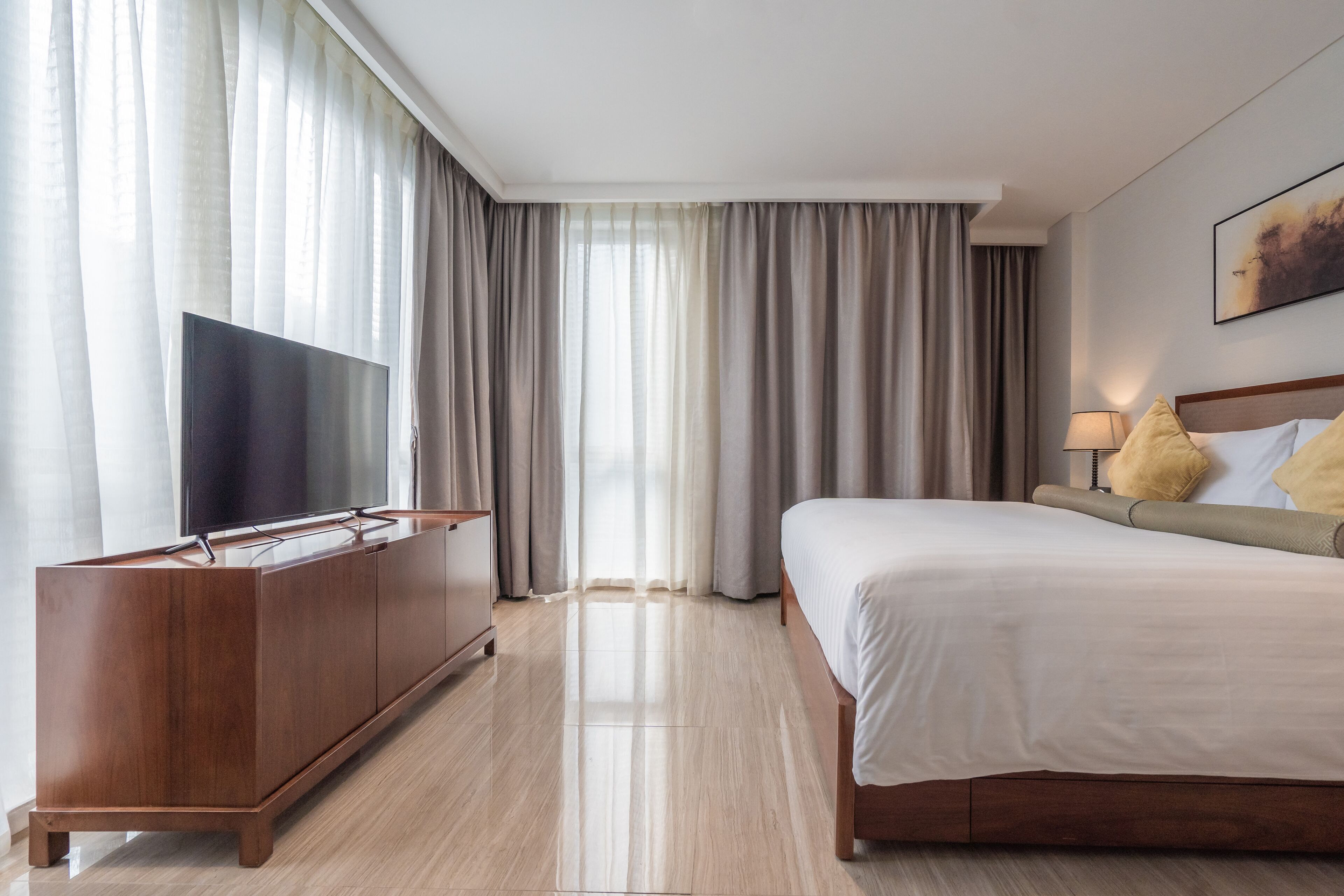 A hotel room with a bed, a TV, a wooden cabinet, and a window with curtains.