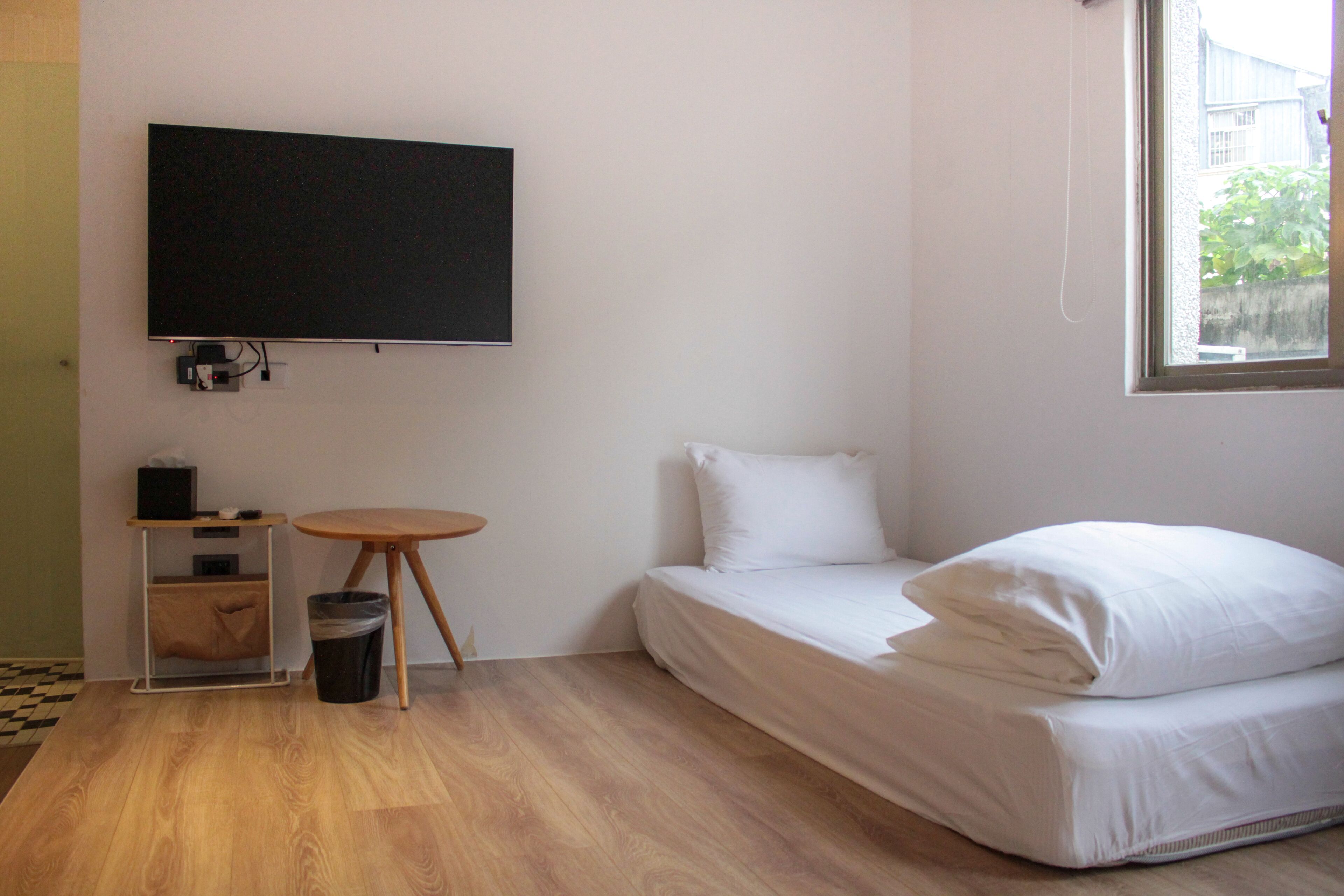 A room with a bed, a TV mounted on the wall, a small table, and a window.