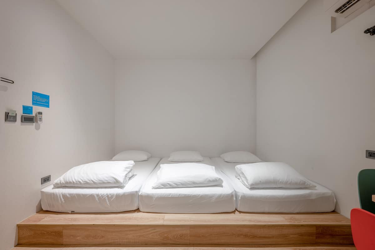Una cama individual con ropa blanca en una habitación de paredes blancas y plataforma de madera.