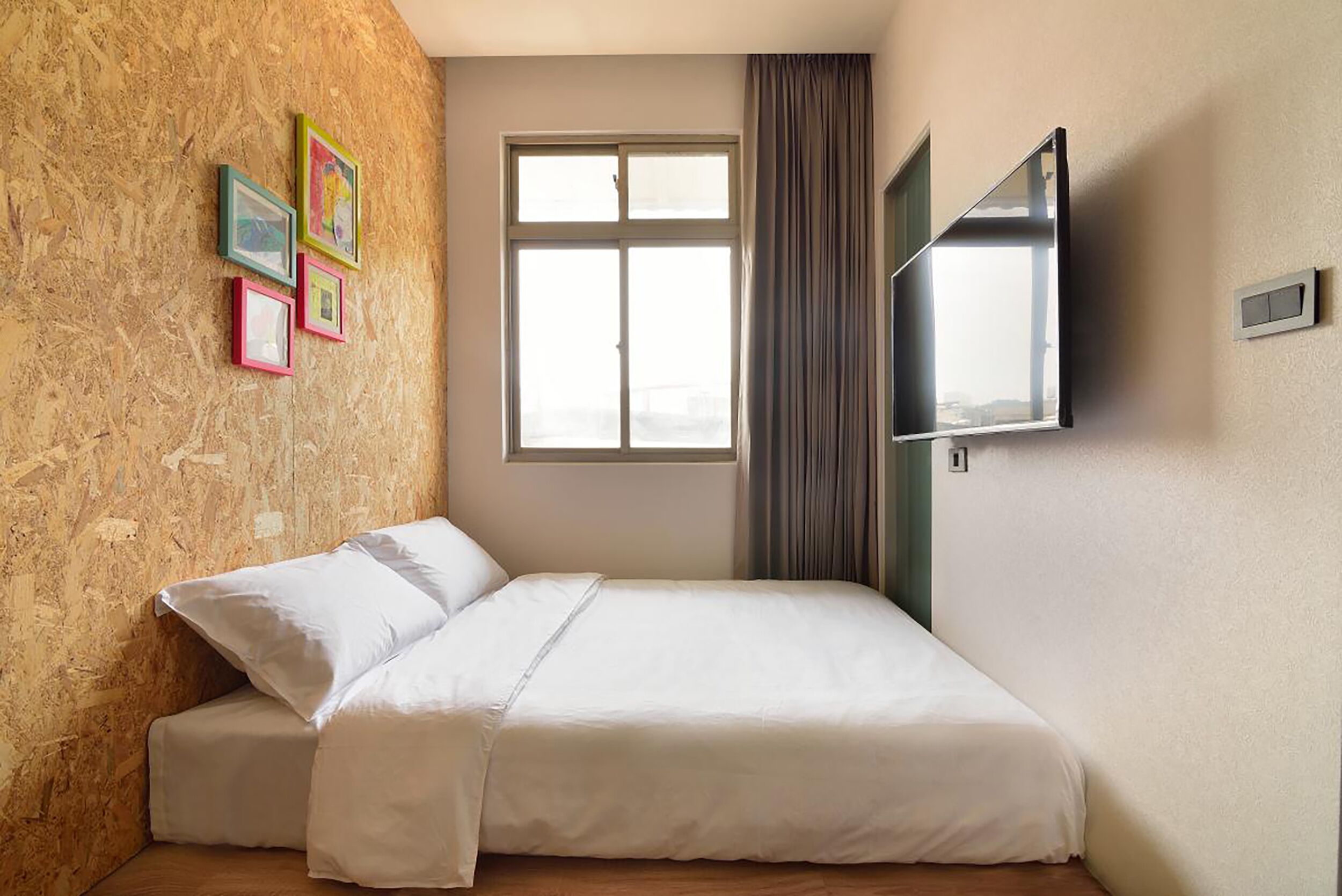 A bedroom with a bed, a window, a TV, and a wall with framed pictures.