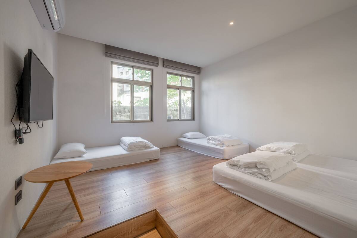 Una habitación moderna y minimalista con dos camas individuales, una mesita de madera y un televisor montado en la pared.