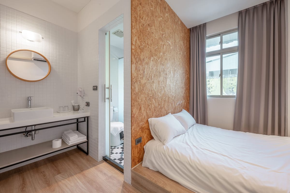Una habitación de hotel moderna con una cama grande, un baño con lavamanos y espejo, y vistas al exterior a través de una ventana.
