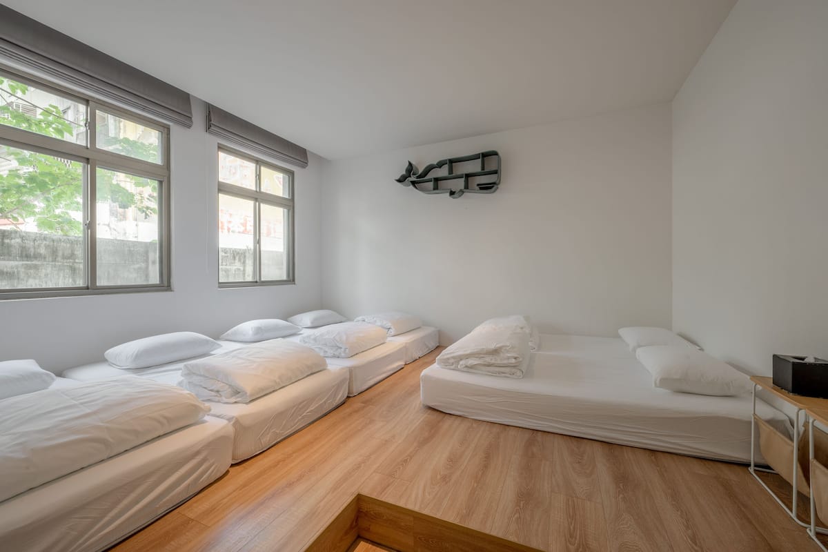 Una habitación con tres camas, suelo de madera y una obra de arte en la pared.