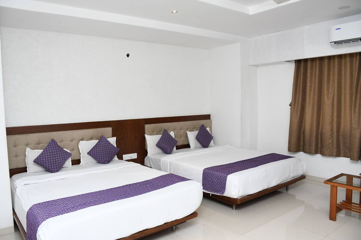 Une chambre d’hôtel avec deux lits simples, une tête de lit en bois, du linge de lit blanc et un rideau marron.