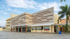 A modern building with a flat roof and a large open plaza in front. - Hotel Pushpak Resort (Rahata)