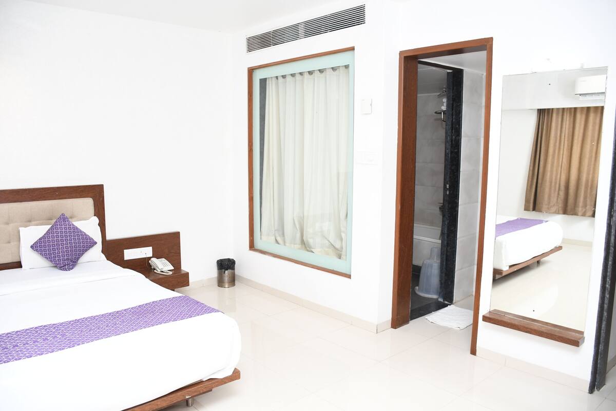 Une chambre d’hôtel comprenant un lit, une table de chevet avec un téléphone, une poubelle, une fenêtre avec des rideaux et un miroir.