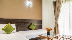 A hotel room with two beds, a glass coffee table, a wooden chair, and a window with curtains. - Hotel Pushpak Resort (Rahata)