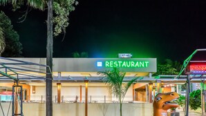 A restaurant with a neon sign, outdoor seating, and a distinctive sculpture. - Hotel Pushpak Resort (Rahata)