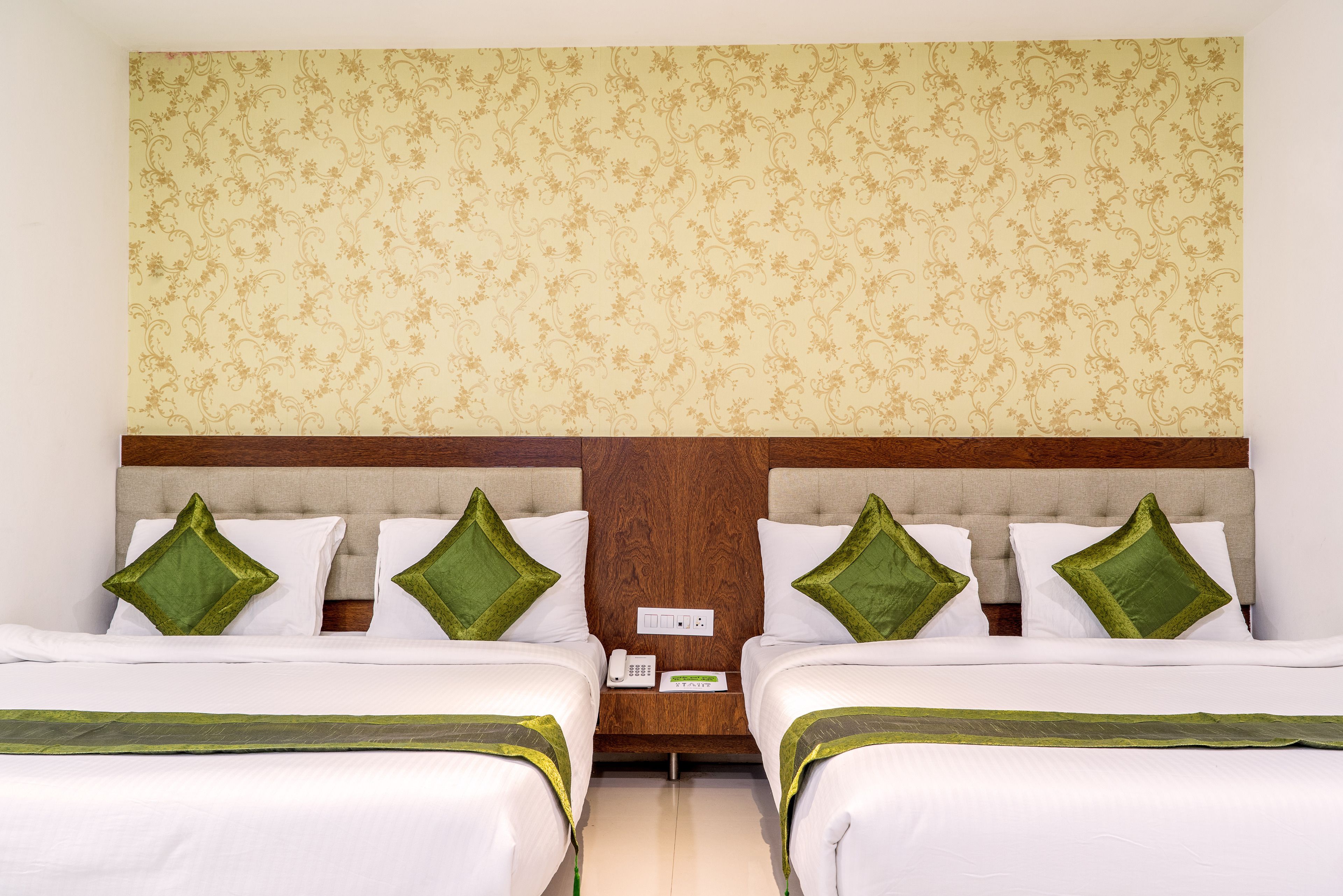 A hotel room with two beds, a wooden headboard, and a floral-patterned wall.