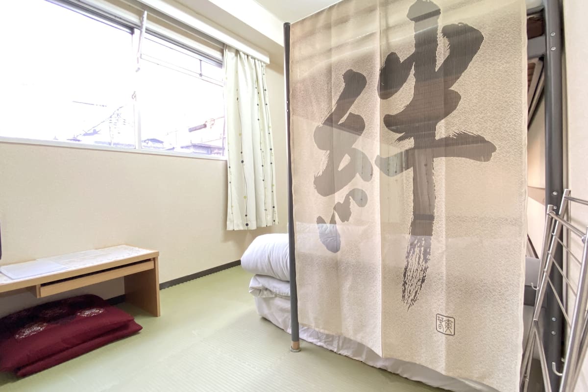 A room with a bed, a desk with a computer, a window with curtains, and a sliding door with a large kanji character.