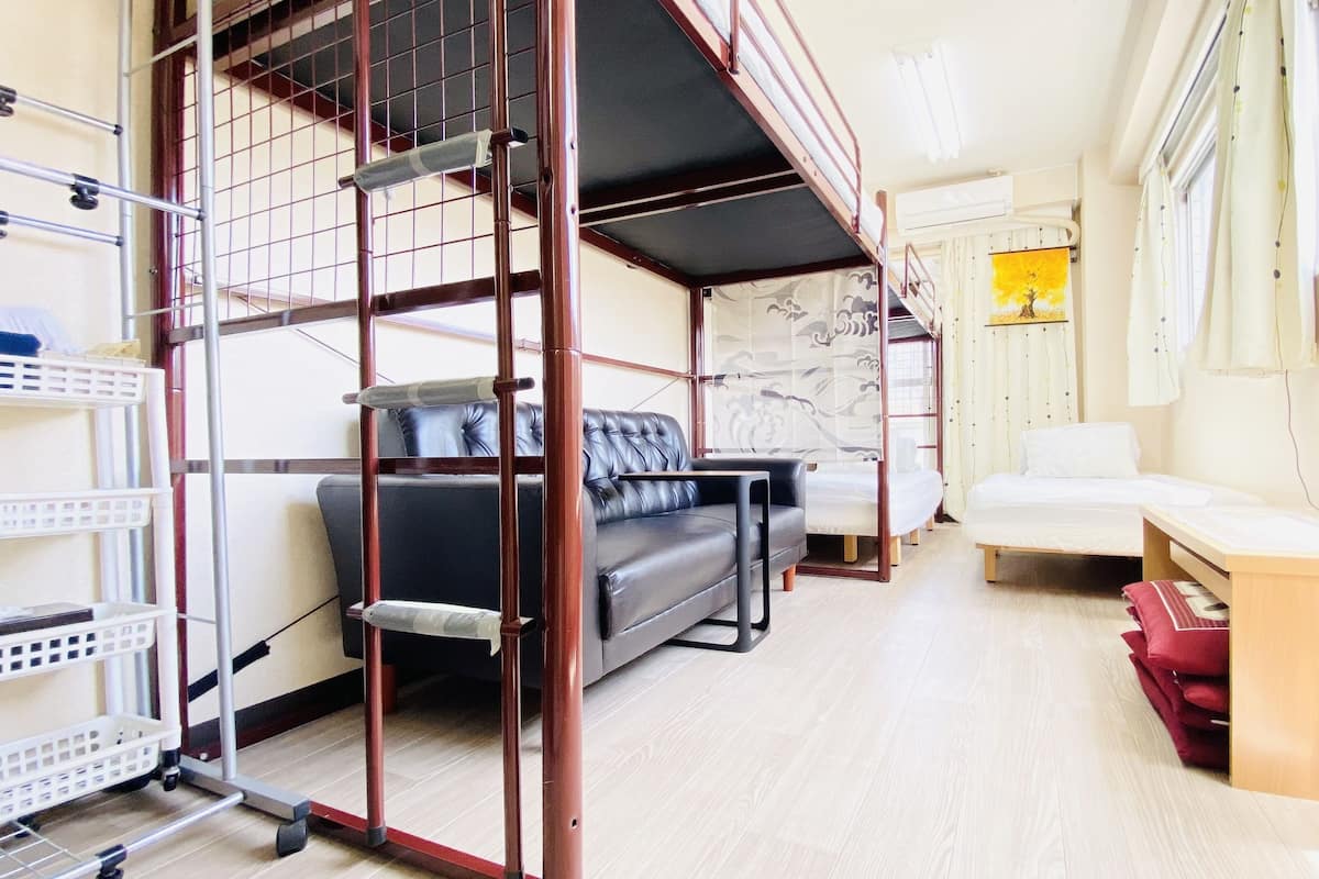 A compact hotel room with a bunk bed, a sofa, a desk with a computer, and a window with curtains.
