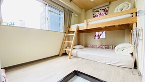 Ein Schlafraum mit Etagenbetten, einer Holzleiter, einem kleinen Fenster mit Vorhängen und einer weißen Bettdecke.