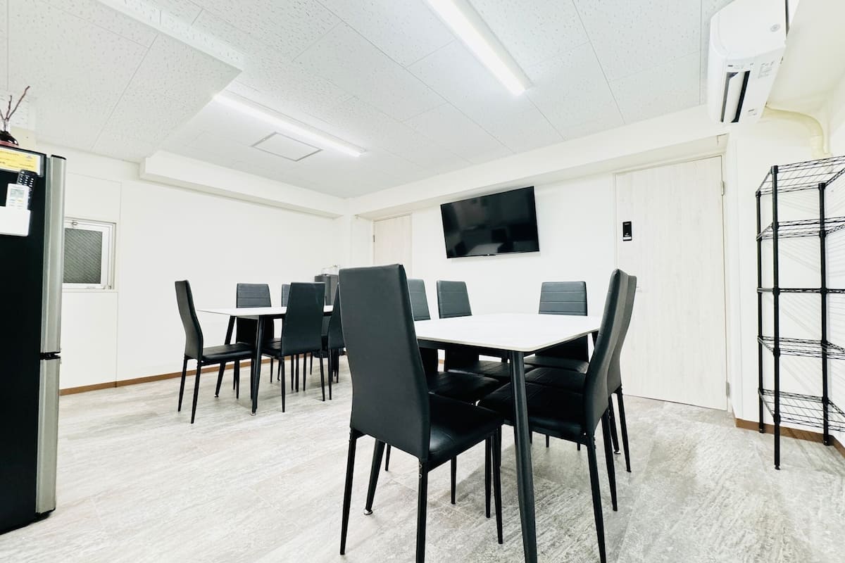 A conference room with a white table and black chairs, a flat-screen TV on the wall, and a black refrigerator.