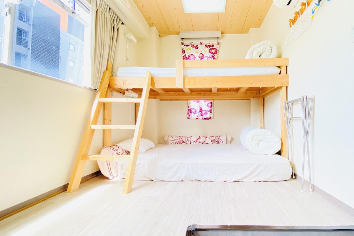 A bunk bed room with a ladder, a small window with floral curtains, and a white door with a handle.