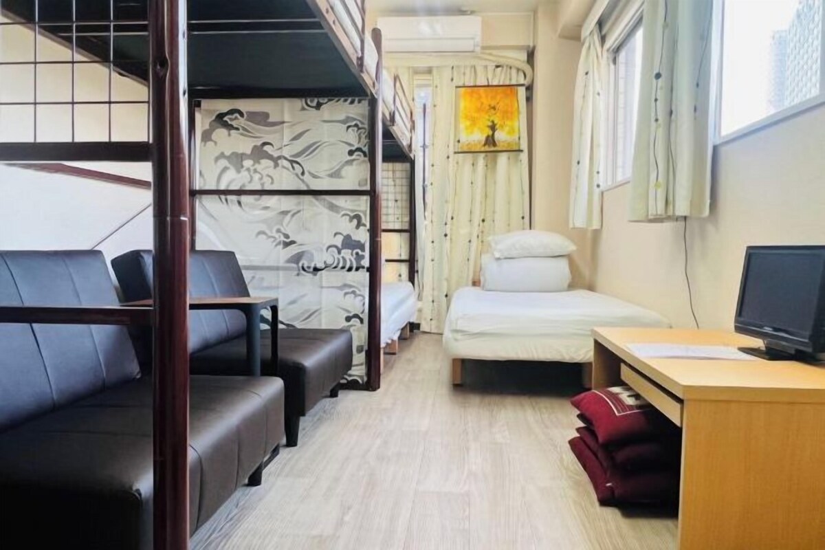 Habitación de hotel compacta con literas, una cama individual, un escritorio con computadora y una ventana con cortinas.