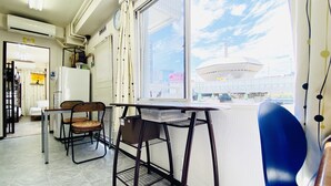 Ein Zimmer mit großem Fenster, einem Tisch, zwei Stühlen und einem kleinen Kühlschrank.
