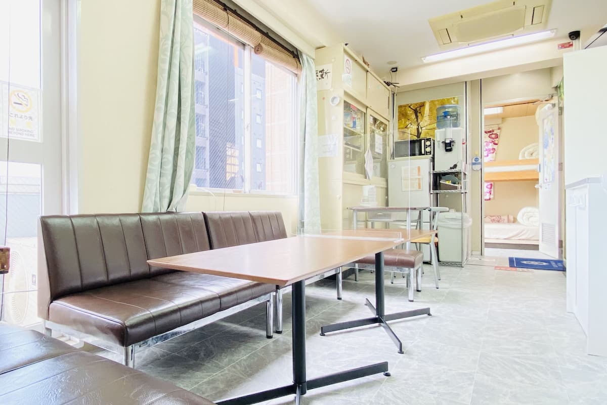 A hotel room with a sofa, a table, a bed, a window with curtains, a water dispenser, and a refrigerator.