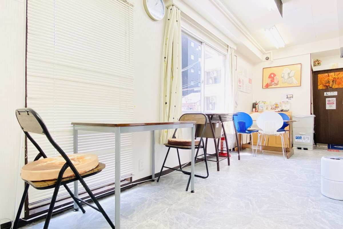 A room with a table, chairs, a window with blinds, a door, and a wall with a clock and a framed picture.