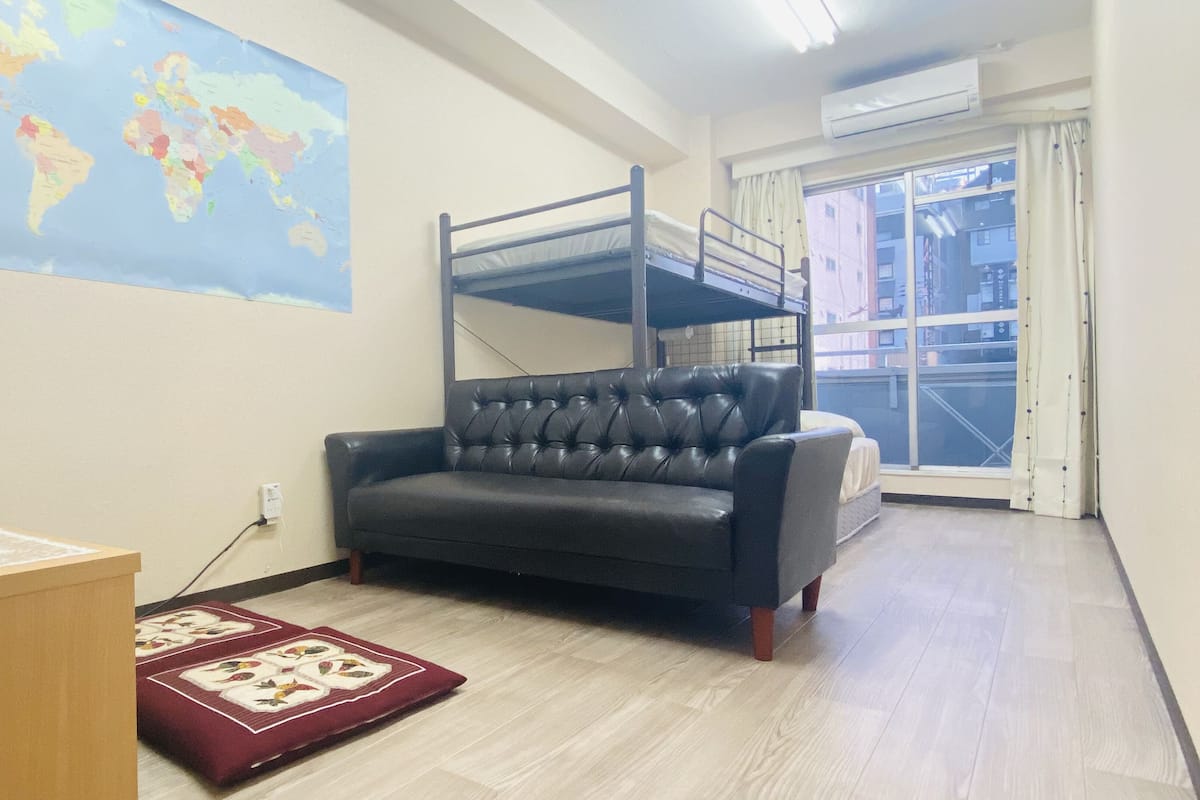 A room with a bunk bed, a leather sofa, a world map on the wall, and a window with a view of buildings.