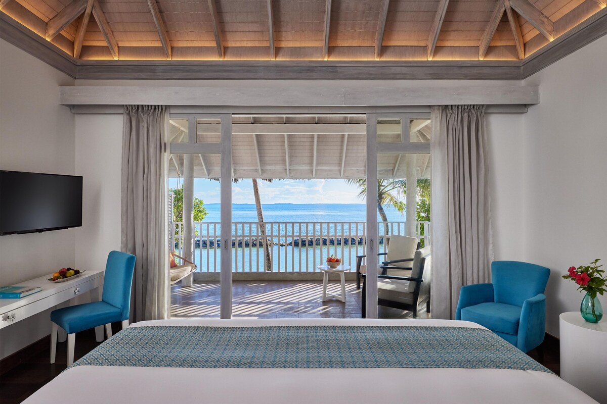A hotel room with a bed, a desk, a chair, a TV, and a view of the sea.