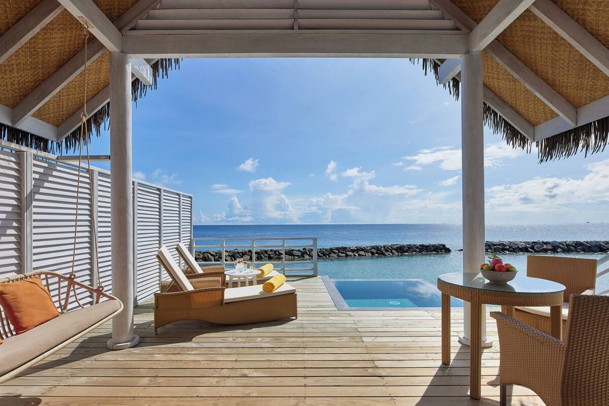 A wooden deck with a pool, lounge chairs, and a table with fruit.