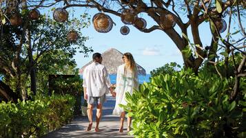 A couple walking on a wooden pathway surrounded by lush greenery and hanging decorative baskets.